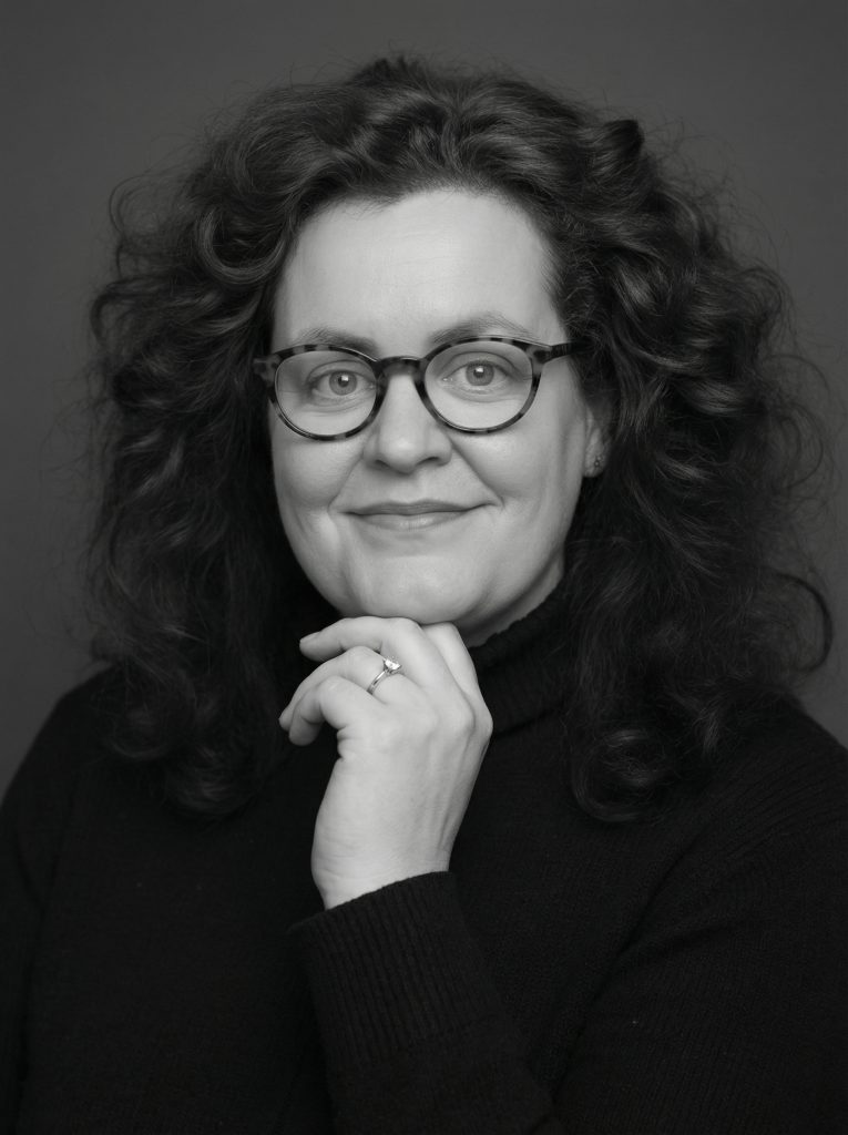 Cornelia Schmitz - Mentorin Cornelia Schmitz - Mentorin, eine Frau mit Brille und lockigem Haar, Sie bickt freundlich und souverän in die Kamera